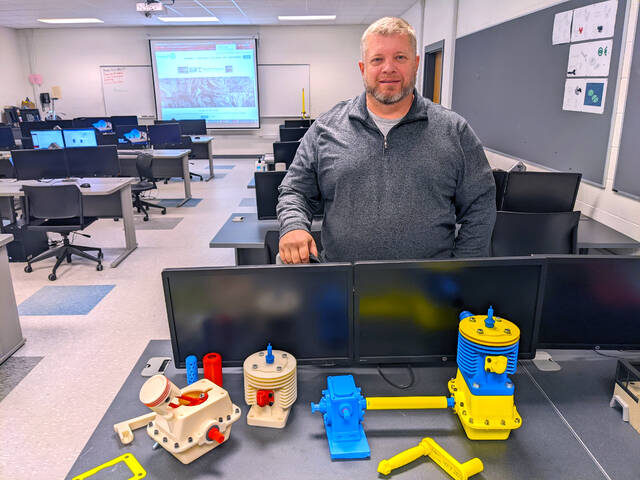 128425947_web1_Robert-Lewis_ME-student
Richmond Community College student Robert Lewis stands with the two different parts of his CAD III project: a small engine and gear housing.
